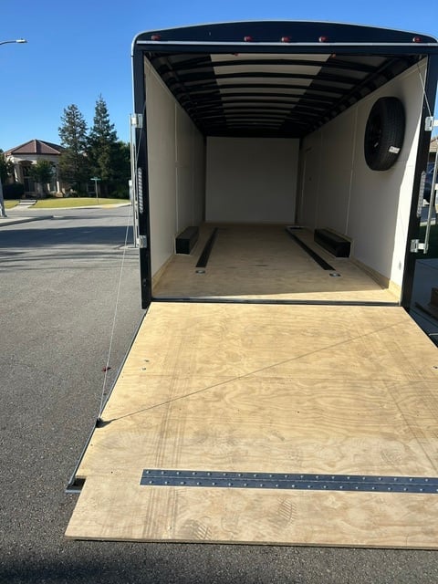 Open empty enclosed cargo trailer with plywood flooring and black interior walls parked on a residential street