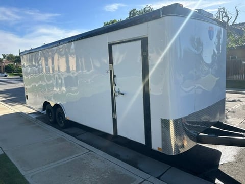 White enclosed cargo trailer with dual axles parked in a lot on a sunny day