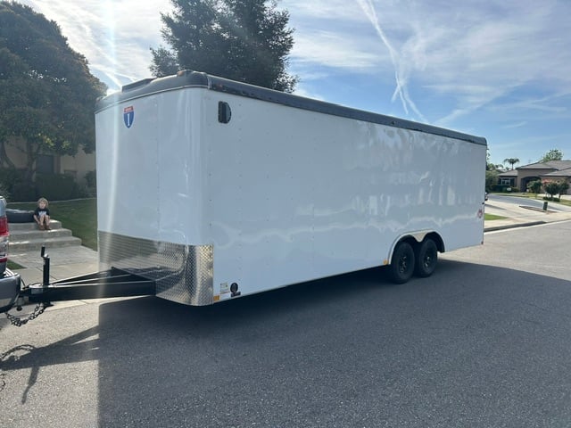 White enclosed cargo trailer with black roof and dual axles parked on asphalt driveway