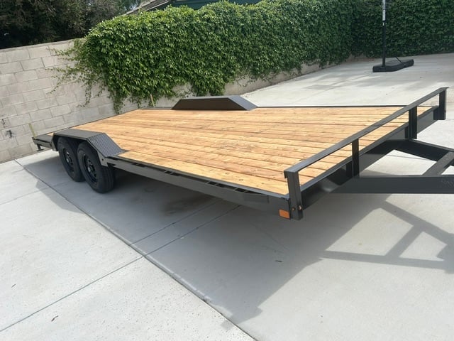 Flatbed utility trailer with wooden deck and black metal frame parked on concrete driveway